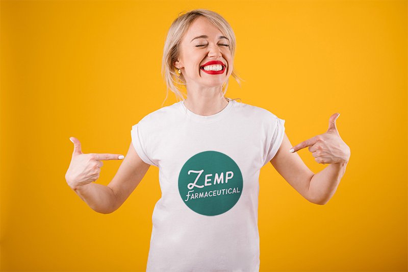 Happy young woman wearing a white t-shirt with a Zemp Farmaceutical logo while standing in front of a yellow wall.