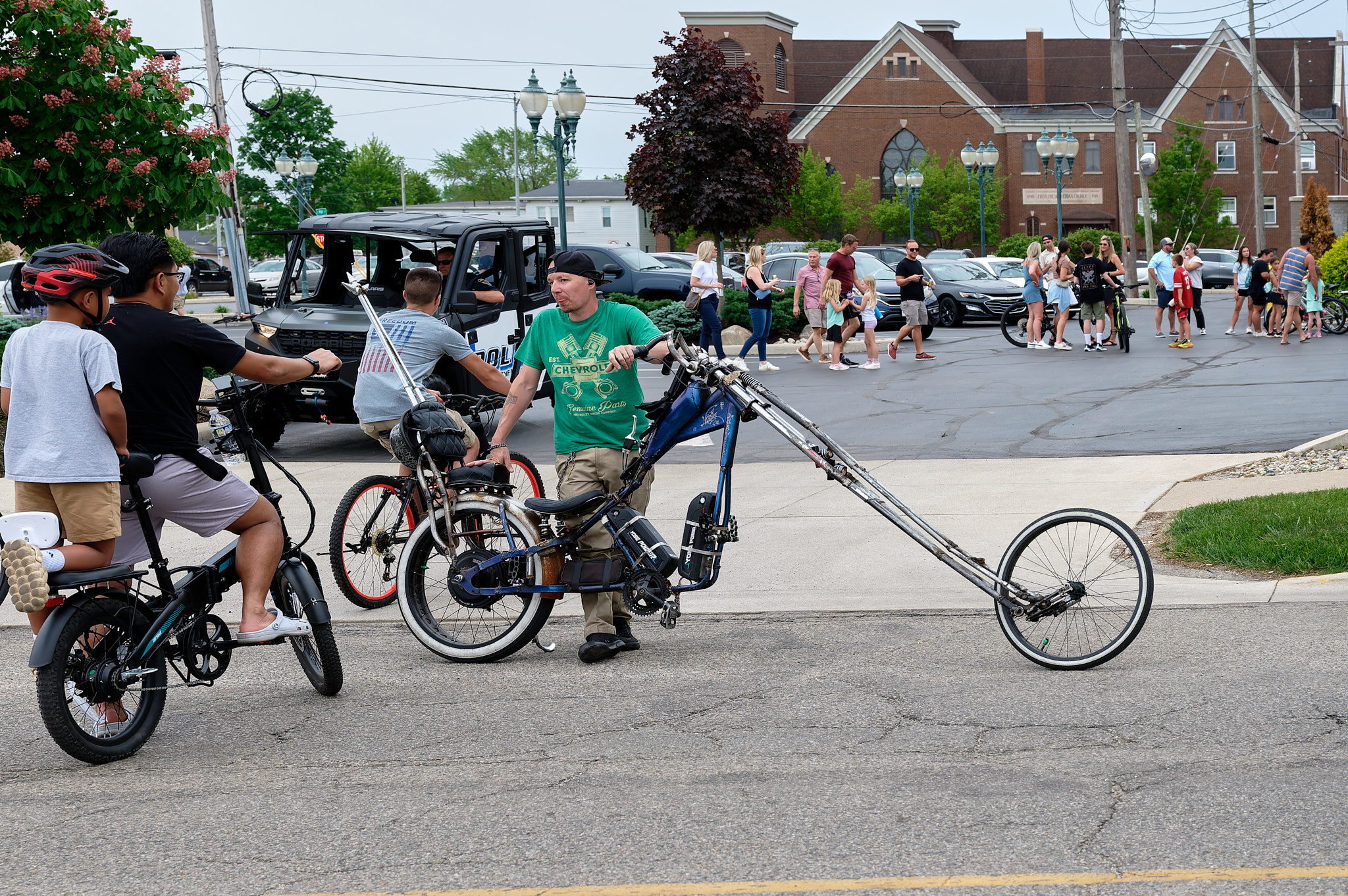 A man standing next to his custom e-bike chopper talking to some passersby in the crowd.