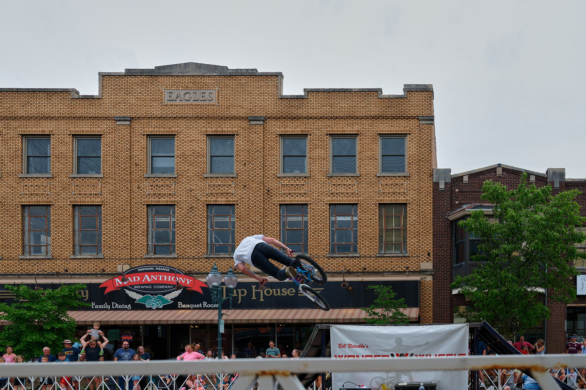 A person on a BMX bike doing a jump trick from a ramp while a crowd watches.