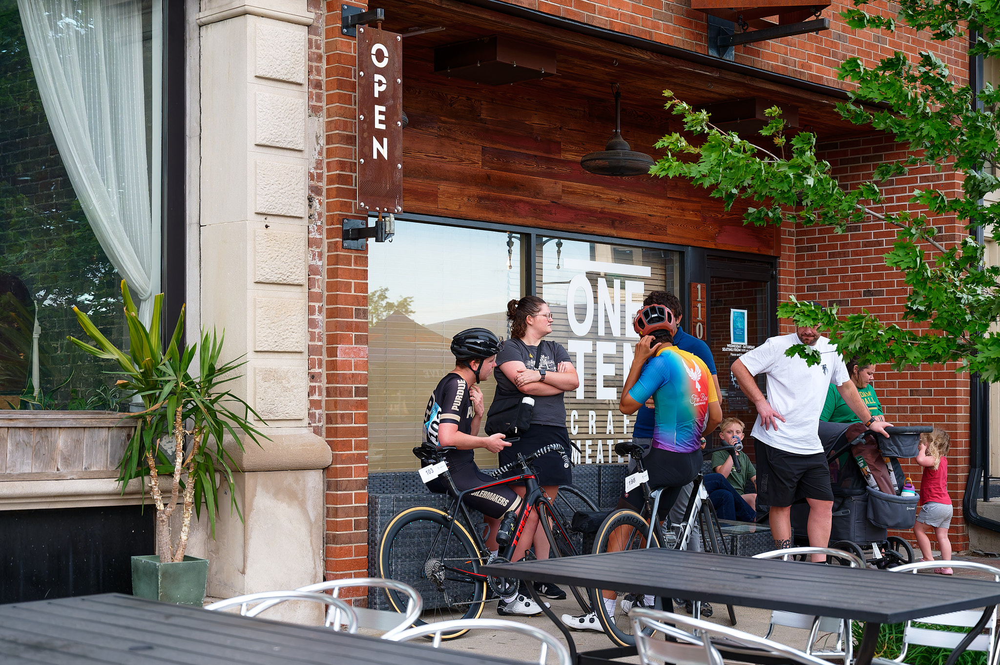 Two cyclists and a few other people wait under a storefront awning for a storm to pass.