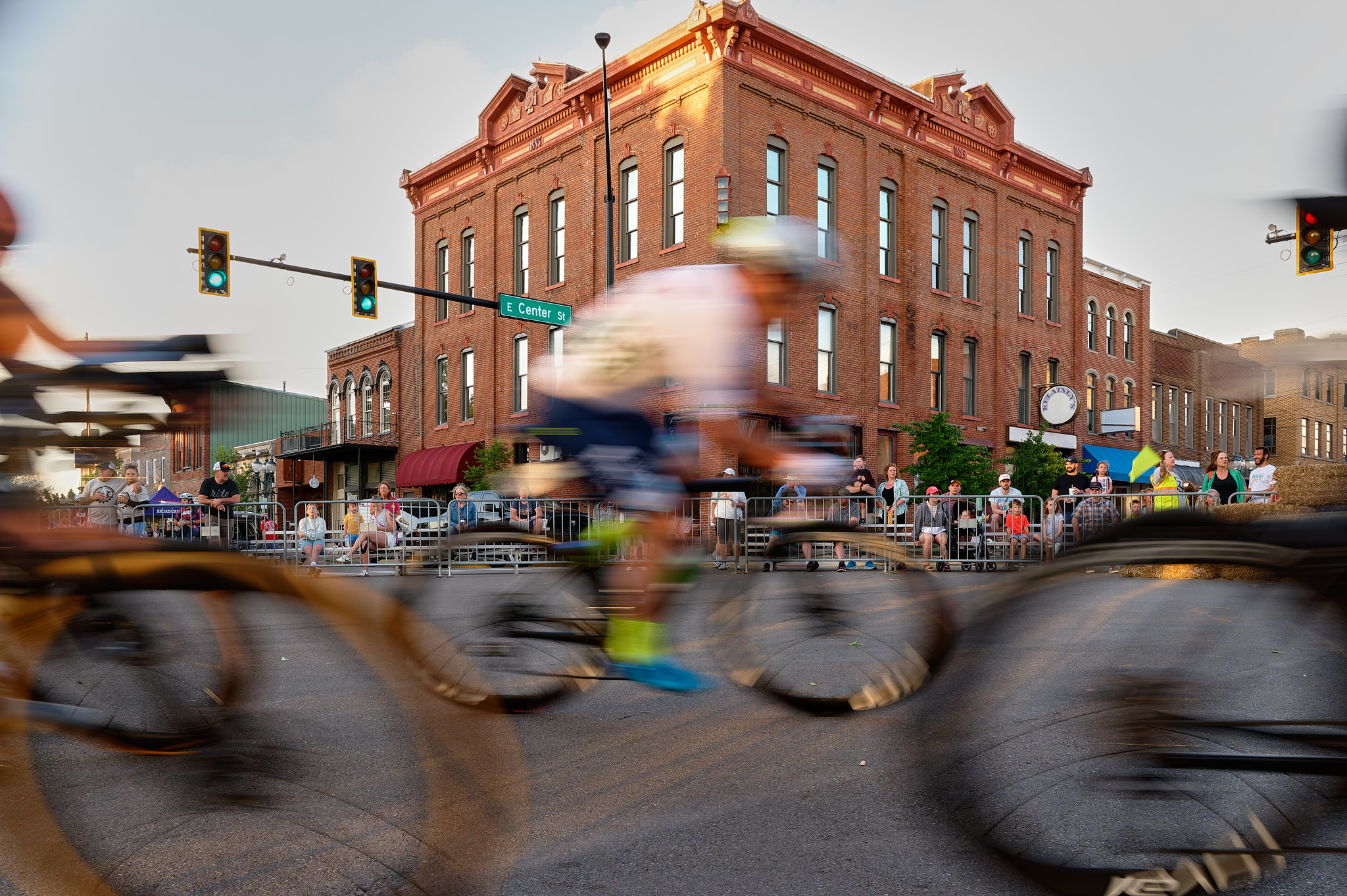 A line of men on bicycles race past as a crowd of spectators watch.