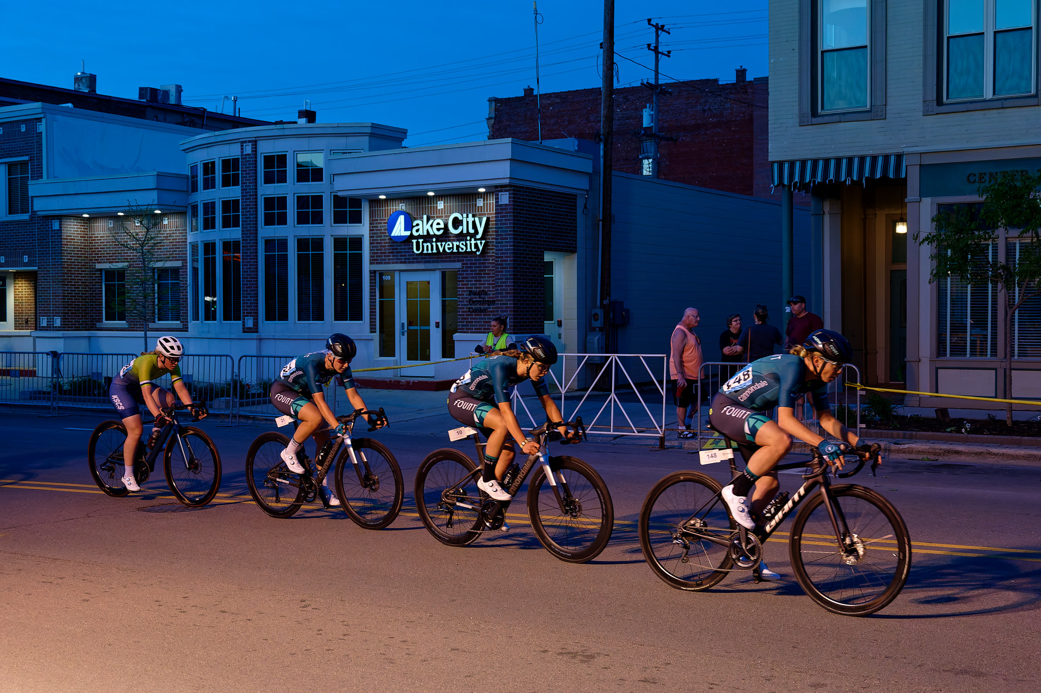 Four women race their bicycles through the streets at dusk.