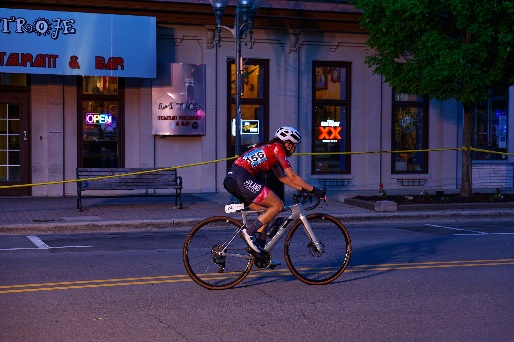 A woman races on her bicycle past a restaurant at dusk.
