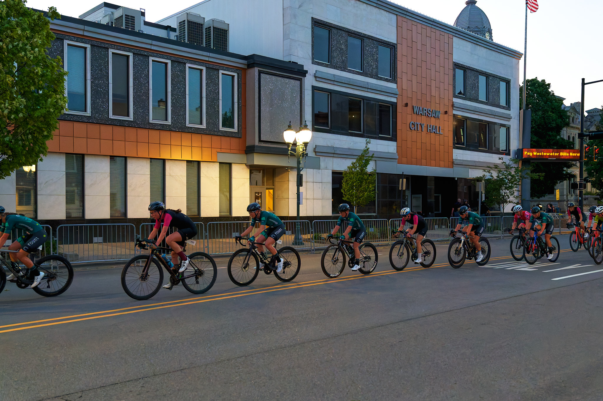 A line of women race their bicycles through the streets at dusk.