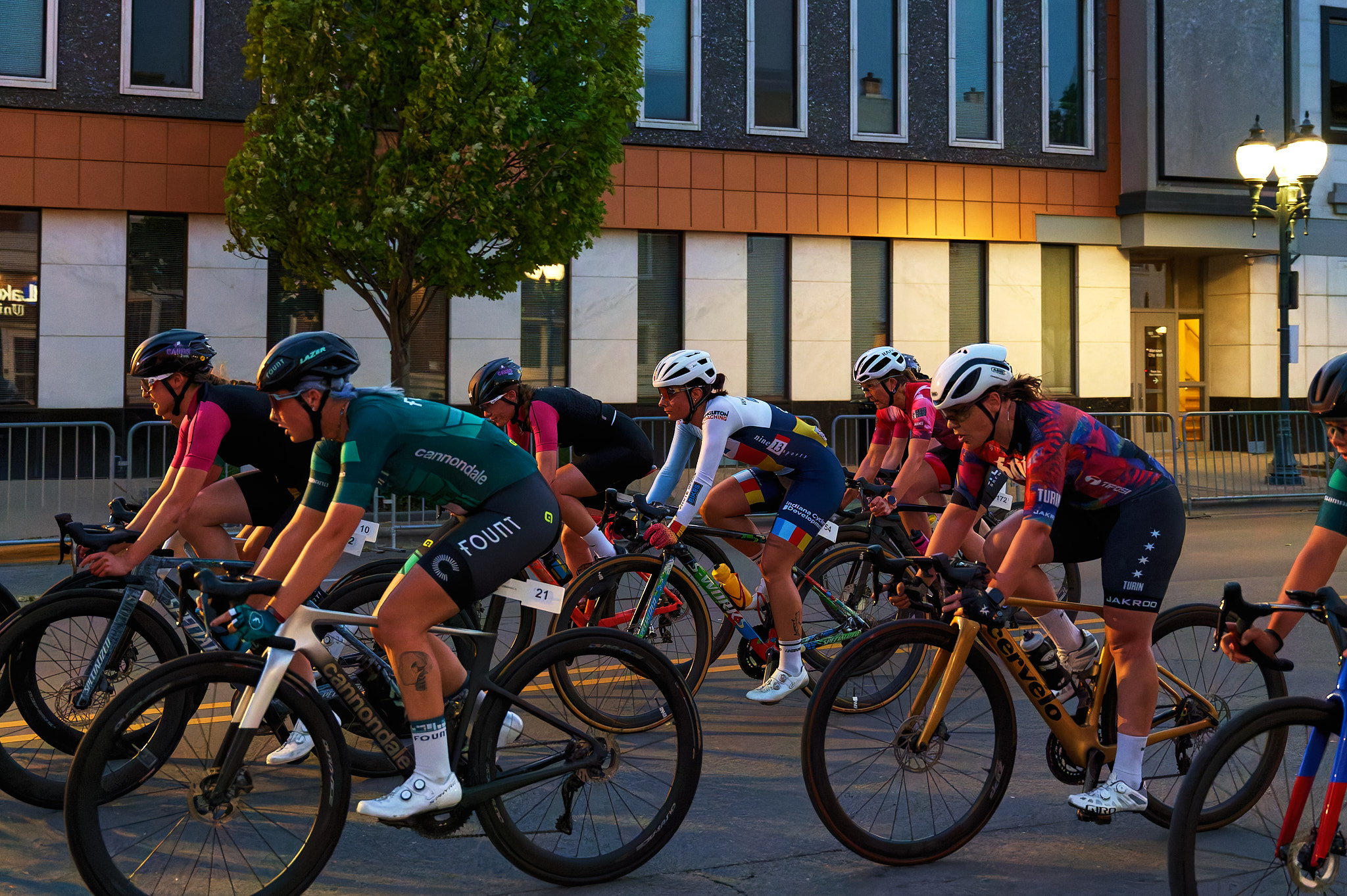 A large pack of women race their bicycles through the streets at dusk.