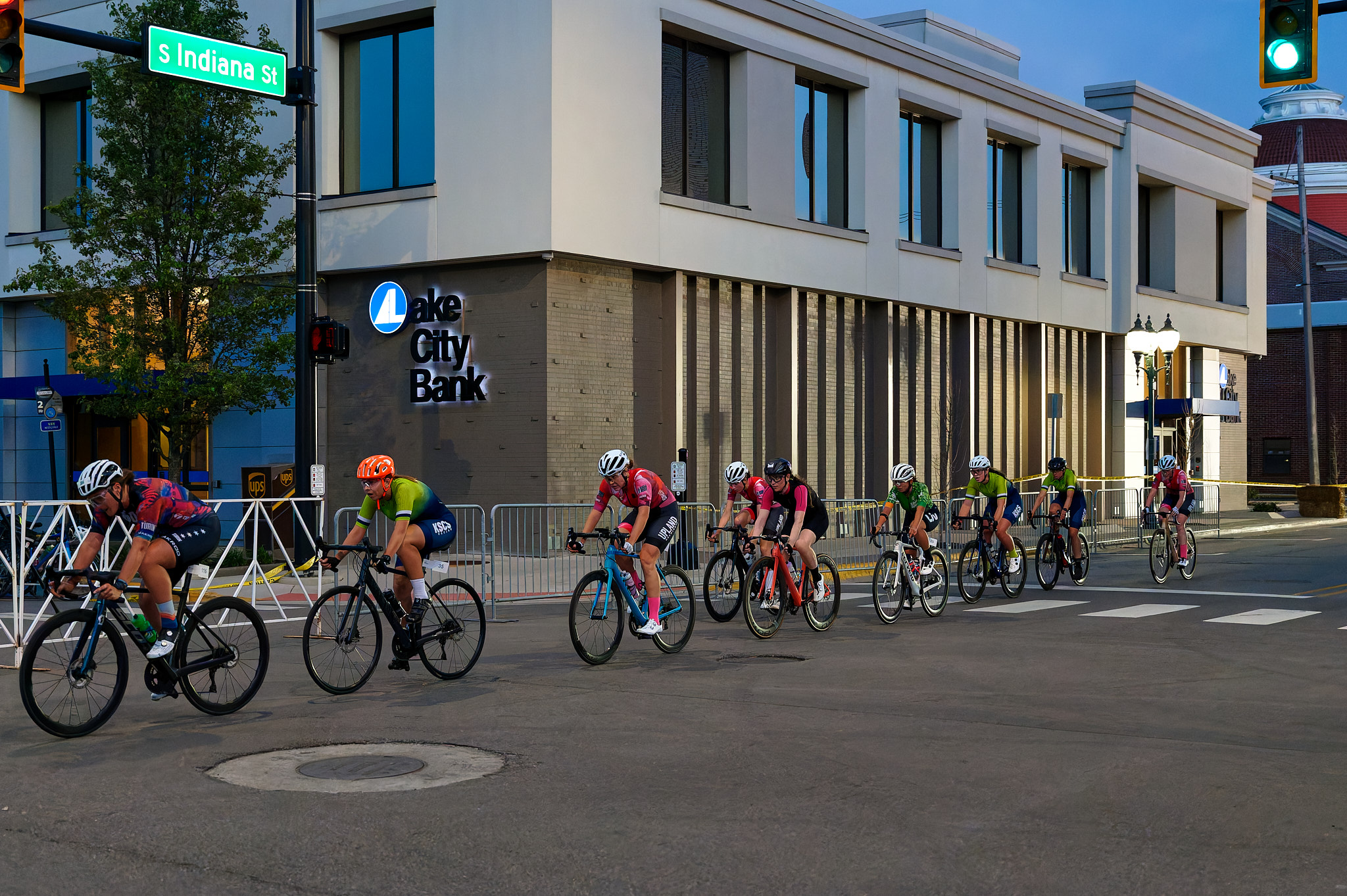 A line of women race their bicycles through the streets at dusk.