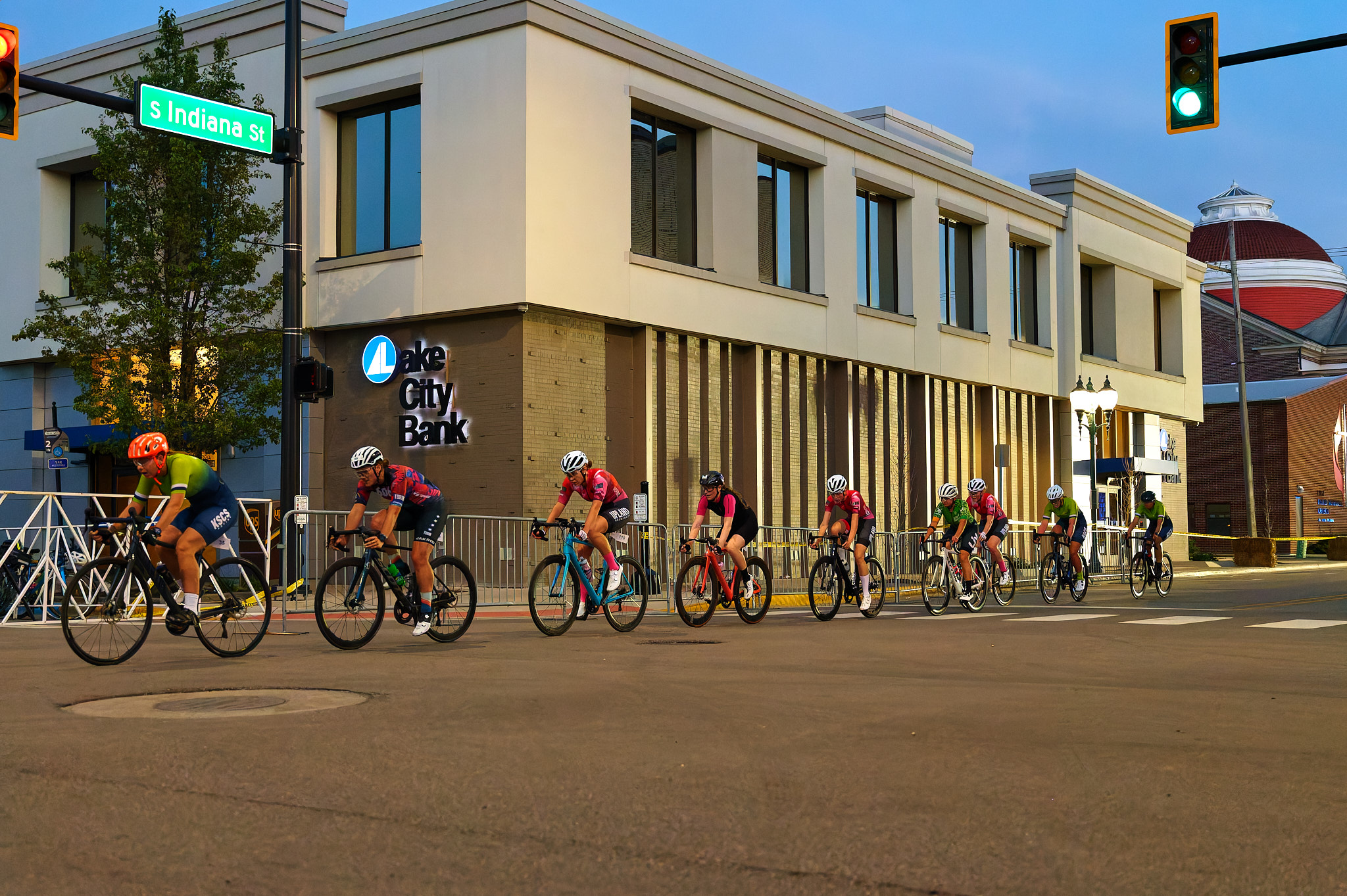 A line of women race their bicycles through the streets at dusk.